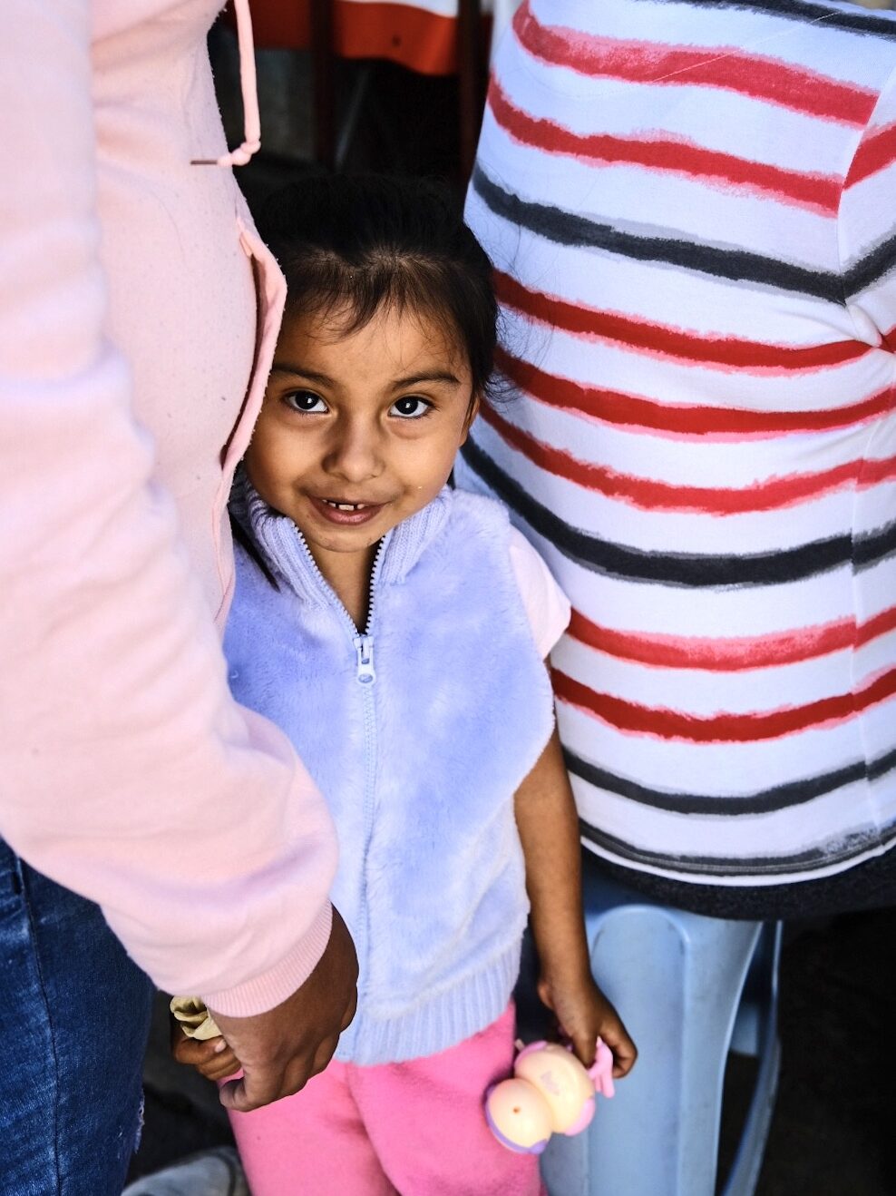 A young girl smiling while standing between two adults